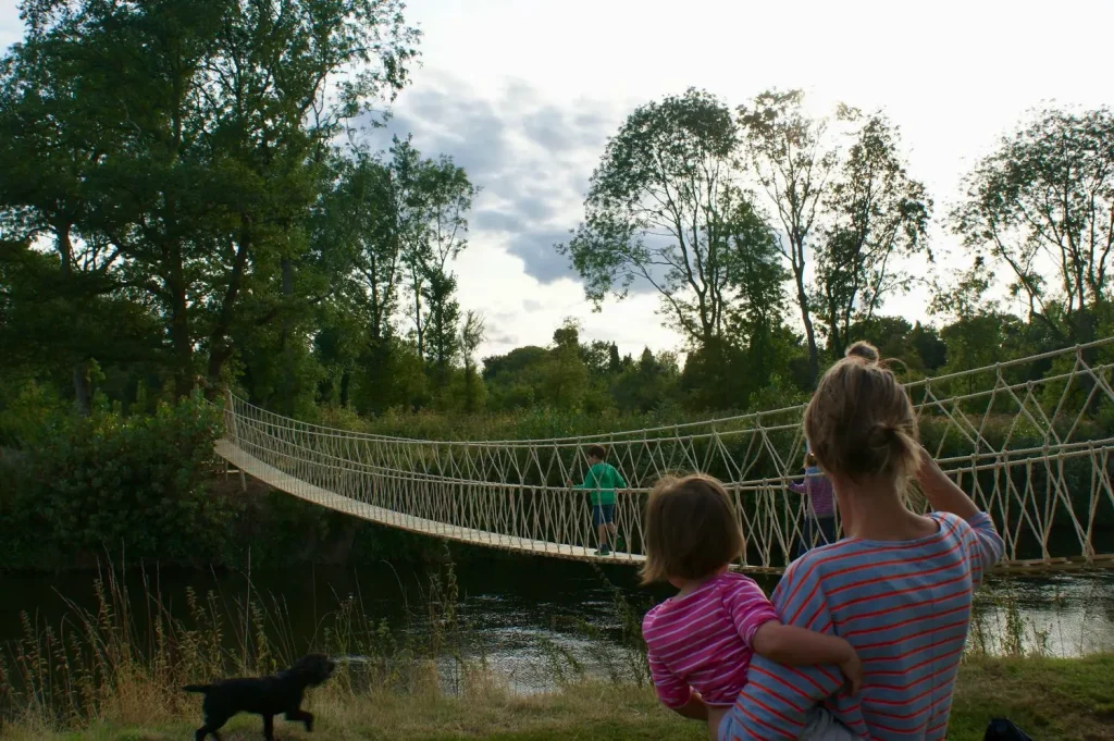 Mother and child watching son walk across o long suspended Rope Bridge over a river