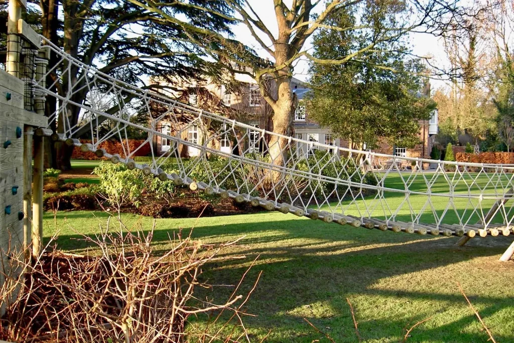 Log Rope Bridge leading to a Treehouse deck in a family garden in front of a large family house