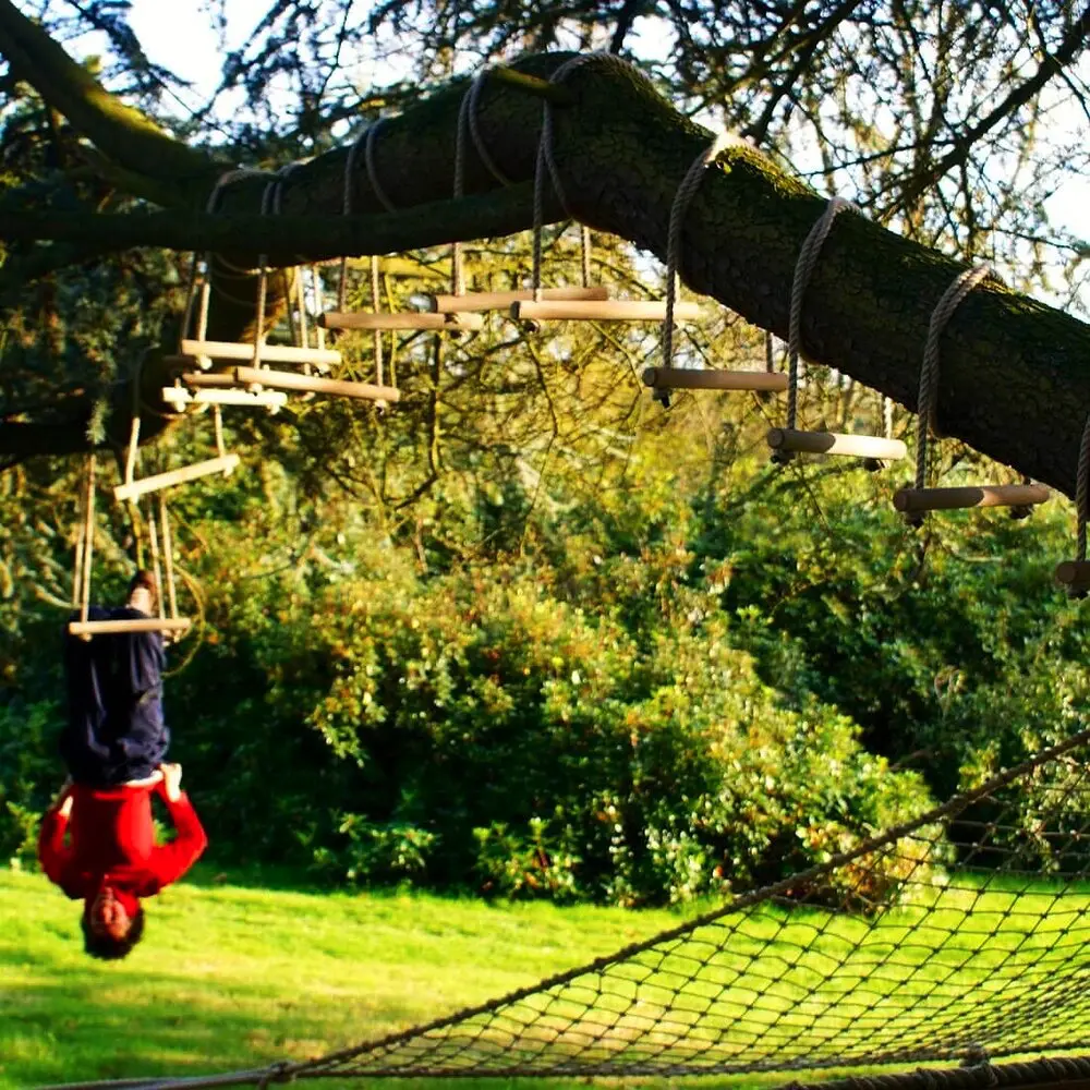 Boy hanging upside down from Monkey Bars install with natural coloured rope to a large tree branch.
