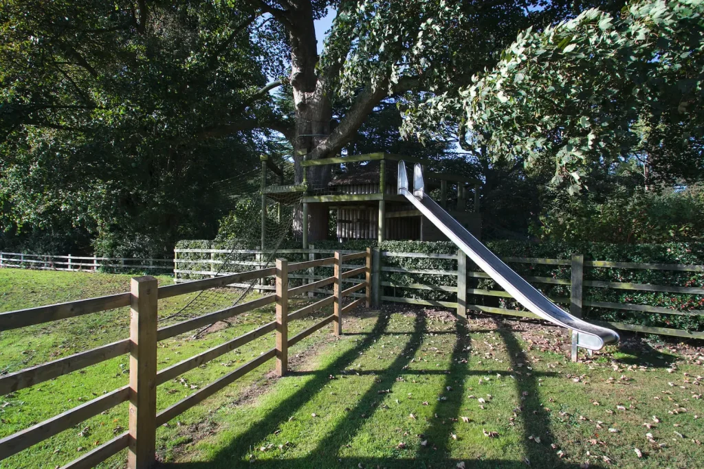 Landscape-architect-treehouse-with-play-options Treehouse set around tree with a large Slide leading into an open garden field.