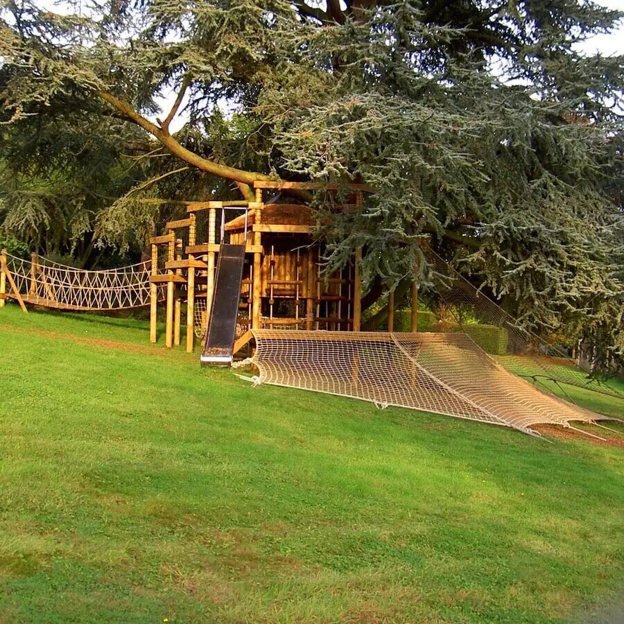 Treehouse set around a large Blue Cedar tree with multiple decks and a large Scramble Net wrapping a deck-platform.