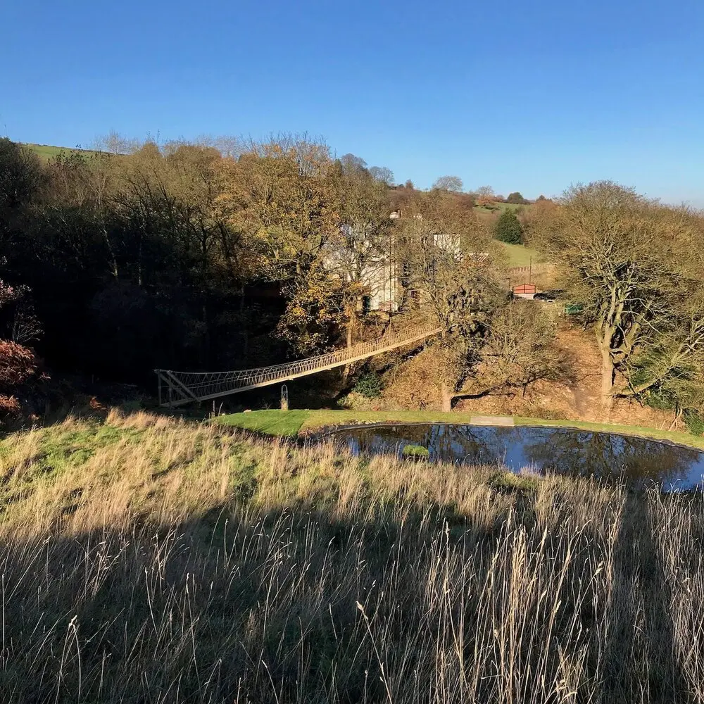 Landscape view across field and lake of a long suspended Rope Bridge