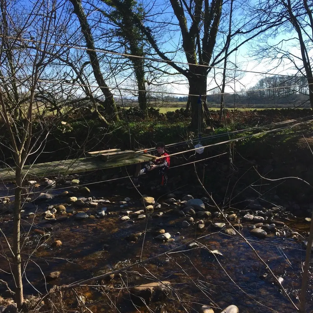 Rope Bridge across a Lake District river with man installing deck board slats.