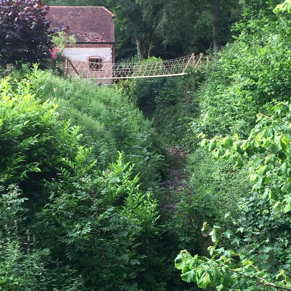 Suspension Rope Bridge over a deep river ravine alongside a water-mill in a family garden.
