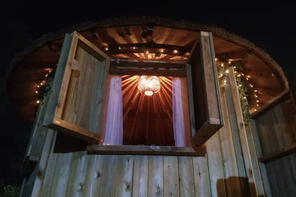 Treehouse at night time, with the windows open and a bright cosy light shinning from inside the treehouse.