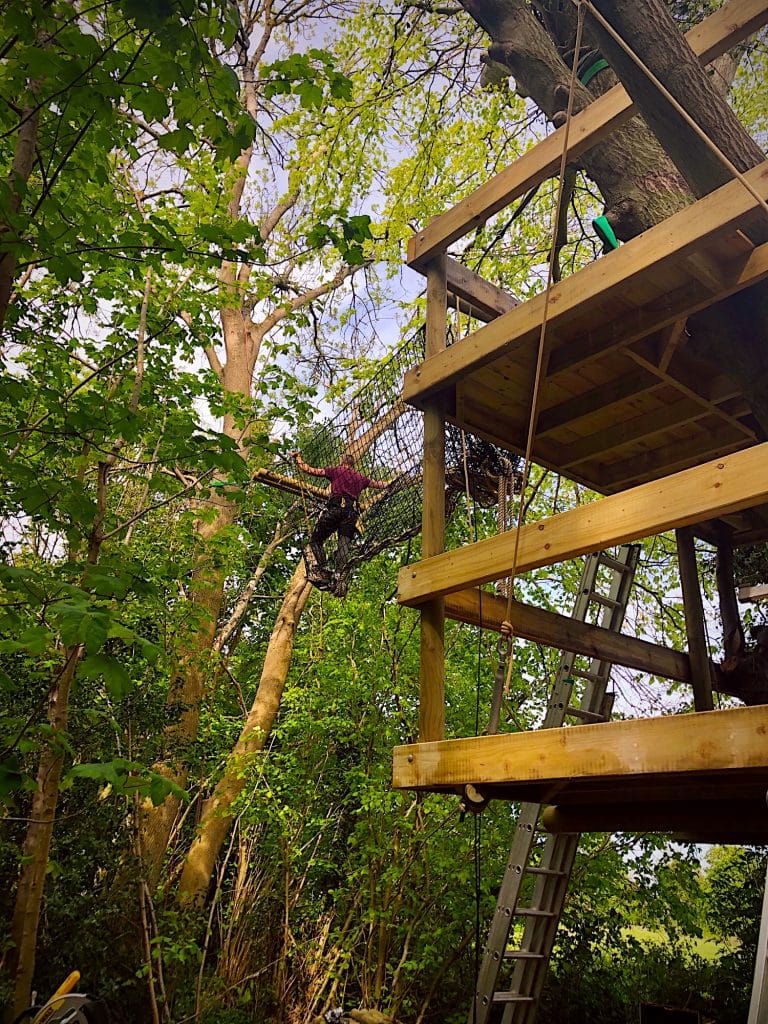 A man across high rope bridge from a double tree deck.