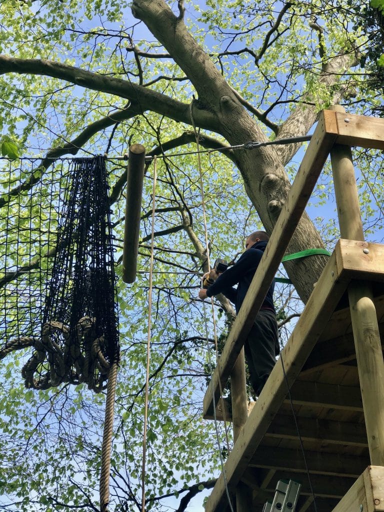 A man hoisting a treetop rope bridge into place.