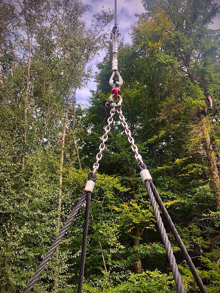 Perspective view looking up at a zip line cable with metal links and rope, ready for an exhilarating ride through a canopy of trees. A close up picture of a rope suspension that forms part of an aerial playground.