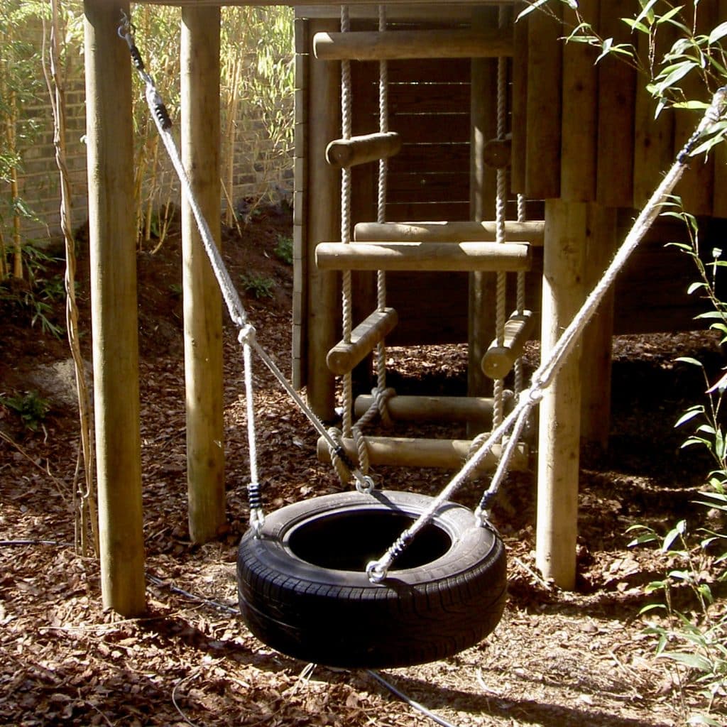 a large tyre swing suspended from a garden treehouse.