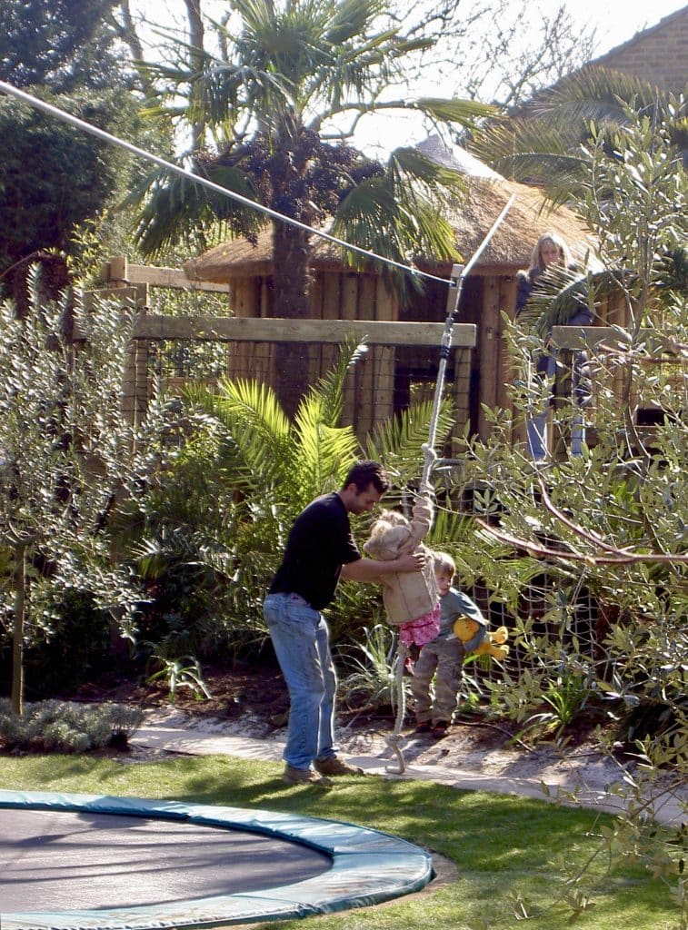 A father helps his young child on to a zip wire in their family garden.